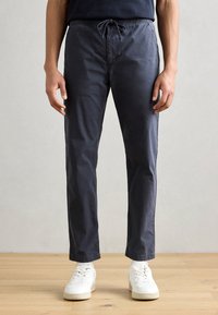 Mörkblåbyxor med elastisk midja och snörning, med rak skärning och slät yta, kombinerat med vita sneakers.