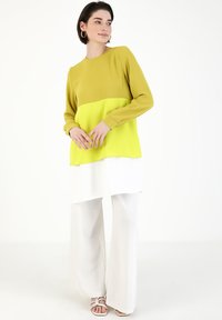Maglietta a maniche lunghe con un design a blocchi di colore giallo e lime. Abbinata a pantaloni bianchi larghi. Il materiale sembra morbido, con una superficie liscia.