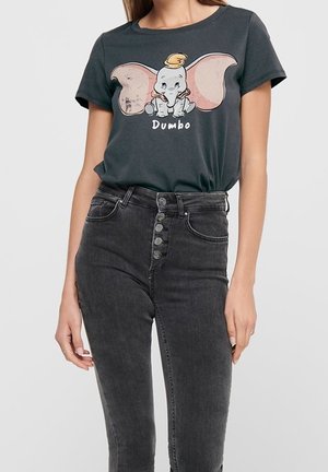 Femme portant un t-shirt graphique Dumbo gris foncé associé à un jean skinny noir taille haute avec braguette à boutons.