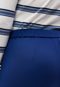 Φόρεμα με άσπρο πουκάμισο με οριζόντιες ρίγες σε μπλε, μαύρο και γκρι, φορεμένο μέσα σε ψηλόμεσο μπλε παντελόνι με ελαστική μέση.