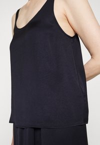 Granatowy, bezrękawnik z luźnym krojem, z okrągłym dekoltem i gładkim, lekkim materiałem. Widoczny detal bocznej panelu.