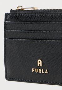 Porte-cartes en cuir noir avec plusieurs emplacements pour cartes, un compartiment zippé et des détails en logo doré. La surface texturée ajoute un intérêt tactile.