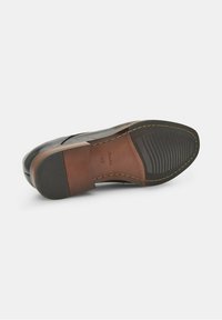 Semelle en cuir noir avec une texture lisse, talon marron et grip en caoutchouc. Détails de couture notables le long du bord. Étiquette de taille visible.