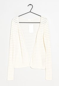 Biała, prążkowana kardigan z długim rękawem i otwartym przodem, wiszący na czarnym haczyku. Metka przymocowana wewnątrz dekoltu. Miękka tekstura.