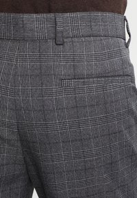 Szare spodnie w kratę wykonane z teksturowanej tkaniny; charakteryzują się slim fit, płaskim przodem oraz jedną kieszenią z tyłu.