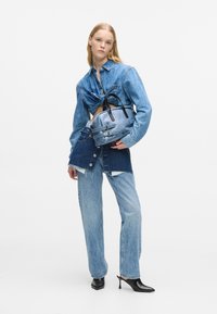 Τζιν πουκάμισο με δεμένο τη μέση, μπλε τζιν και μπλε τσάντα με μαύρα αξεσουάρ και λουριά. Διαθέτει κοντό, πολυεπίπεδο σχέδιο.