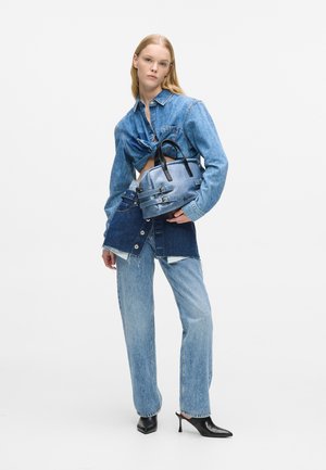 Koszula dżinsowa z przewiązanym w pasie, niebieskie dżinsy oraz niebieska torebka z czarnym wyposażeniem i paskami. Posiada krótki, warstwowy fason.