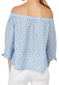 Top azzurro chiaro, scollato sulle spalle con scollatura arricciata e maniche a 3/4. Presenta un motivo di piccole macchie blu navy. Tessuto morbido e intrecciato.