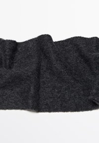 Tessuto morbido di un grigio scuro con una superficie testurizzata e pelosa, drappeggiato e leggermente sovrapposto, che mostra fibre naturali e bordi irregolari.