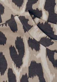 Tissu avec un motif animalier irrégulier marron foncé et beige, montrant une couture d’ourlet pliée.