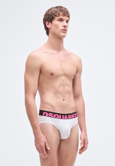 Calzoncillos masculinos blancos con una cintura negra que muestra el logo "DSQUARED" en rosa. La tela parece suave y ajustada al cuerpo.