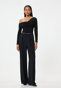 Sort off-shoulder top med lange ærmer, lagdelt design. Kombineret med højtaljede sorte bukser med bred ben, glat stof, plisseret front.