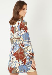 Vestido con estampado floral, de mangas largas, cintura ceñida y una paleta de colores azul, marrón y crema. Fabricado en tejido ligero.