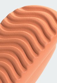 Suola di scarpa color pesca con motivi a onde testurizzati e creste rialzate, che mostra un materiale liscio simile alla gomma e bordi arrotondati.