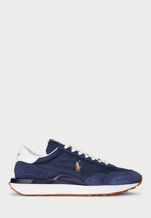 Navy blue sneaker with white laces, white heel collar, orange logo of polo player, white midsole, and orange-brown outsole on neutral background.