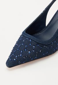 Navy blue slingback pump with pointed toe, textured fabric surface, embellished with blue crystals in a geometric pattern.