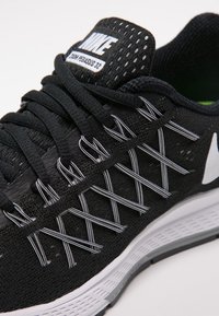Baskets de course Nike noires avec une tige texturée, des accents blancs, un bout arrondi et une semelle rembourrée. Présente des lacets entrecroisés et un logo.