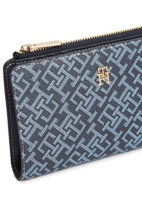 Πορτοφόλι με φερμουάρ σε σκούρο μπλε χρώμα με ένα σχέδιο σε ανοιχτό μπλε. Διαθέτει χρυσό λογότυπο και λείο υλικό. Σχηματισμένο σε ορθογώνιο, δομημένο σχήμα.