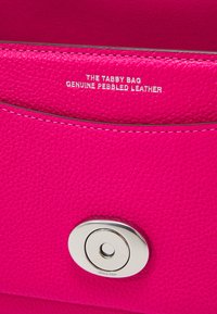 Fuchsia pebbled leather handbag with silver hardware, featuring a round snap closure and embossed text reading "THE TABBY BAG GENUINE PEBBLED LEATHER."