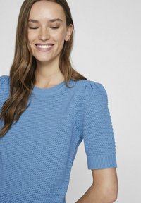 Světle modrý pletený svetr s krátkými nafouknutými rukávy, žebrovanými manžetami a texturovaným designem. Měkká látka, kulatý výstřih a přiléhavý střih.