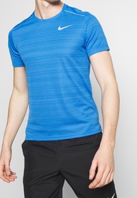 Blå Nike träningströja med ett strukturerat randigt mönster, korta ärmar och en vit Nike-logotyp på vänster bröst. Slät tyg.