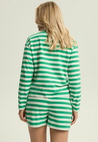 Zestaw odzieży casualowej w zielono-białe paski, składający się z długiego rękawa i szortów. Miękka tkanina o luźnym kroju, gładkiej fakturze i swobodnym designie.