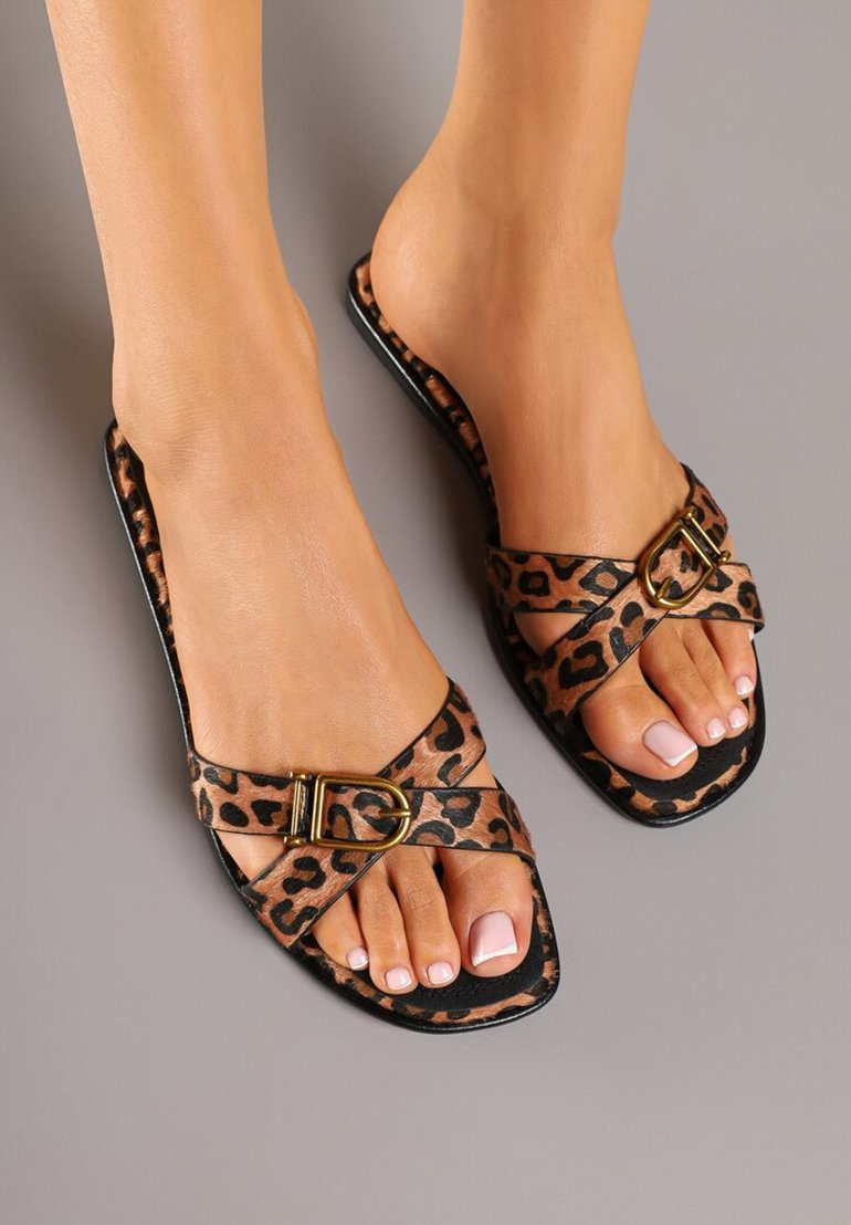 Sandales plates en imprimé léopard avec un design à brides croisées, mettant en valeur une boucle dorée. Fabriquées en matériau synthétique texturé dans des teintes beige et noir.