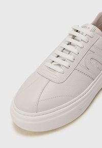 Sneaker in pelle grigia chiara con superficie testurizzata, punta rotonda, lacci bianchi e suola in gomma. Presenta un design cucito e un logo sul lato.