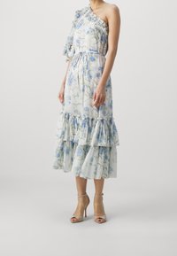 Robe florale à épaules dénudées en tissu léger blanc orné de fleurs bleues. Présente un ourlet froncé et deux volants au bas.