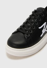 Black leather sneaker with white accents, round toe, contrasting sole, and prominent lace-up design. Features embroidered logo on the side.