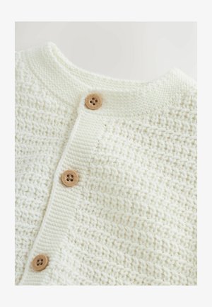 Kremas spalvos megztas kardiganas su tekstūrinio rašto raštu, priekyje trys mediniai mygtukai ir apvalus iškirptės kaklas. Minkšta ir jauki medžiaga.