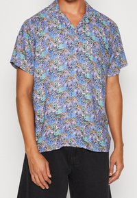 Korte mouw shirt in lichtblauw met abstracte patronen in roze, zwart en groen. Gemaakt van lichte stof met een puntige kraag.