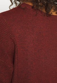 Bordeauxfarbener Strickpullover mit strukturierter Oberfläche, rundem Ausschnitt und dezenten Nähdetails, der ein gemütliches Design veranschaulicht.