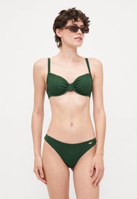Mörkgrön bikini med ribbad textur; bh med underwire och tunna remmar, matchande låg midja; liten detalj i guld vid höften.