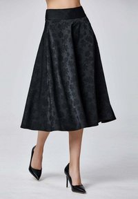 Jupe midi noire en forme A avec un motif floral, en tissu texturé, et une large taille, accompagnée de talons noirs pointus.
