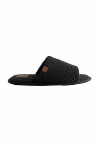 Chaussons noirs avec une tige texturée et matelassée, design à bout ouvert et semelle plate. Une petite étiquette marron accentue le côté.