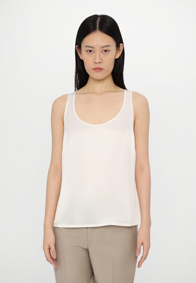 Débardeur élégant en crème légère avec des bretelles larges, un col rond, une texture lisse et une coupe décontractée ; associé à un pantalon de couleur neutre.