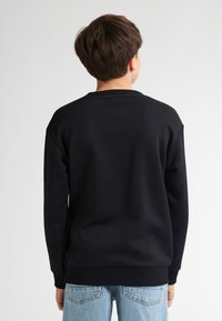 Sudadera negra con cuello redondo, puños acanalados y un ajuste relajado. Tejido suave y textura lisa, combinada con unos vaqueros de un azul claro.