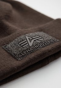 Smeđi pleteni šešir s teksturiranim sivim flasterom na kojem su utisnuti crni tekst i logo. Mekan materijal s prilagođenim dizajnom.