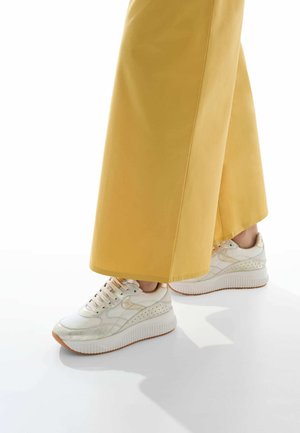Cream sneakers with textured leather, perforated accents, and a thick white sole. Paired with loose, yellow wide-leg pants.