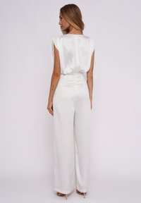 Weißes Satinoberteil mit kurzen Ärmeln und Bindedetails, kombiniert mit hoch taillierten, weit geschnittenen weißen Hosen. Glatte Textur, minimalistisches Design.