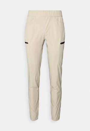 Pantalon slim beige clair avec taille élastique et poches zippées sur les deux cuisses, présenté sur un fond uni.