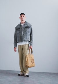 Jachetă din denim gri, scurtă, cu buzunare frontale, tricou alb, pantaloni cargo bej și geantă de umăr bej cu design de lup. Încălțămintea casual completează look-ul.
