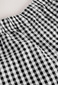 Schwarz-weiß kariertes Baumwollgewebe mit einem gerafften Bund, das kleine Quadrate und eine leicht strukturierte Oberfläche aufweist.