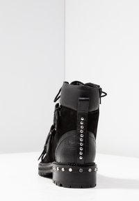Stivale alla caviglia nero in suede e pelle lucida con effetto coccodrillo. Accentuato da borchie argentate attorno alla suola e sul retro. Chiusura con lacci.