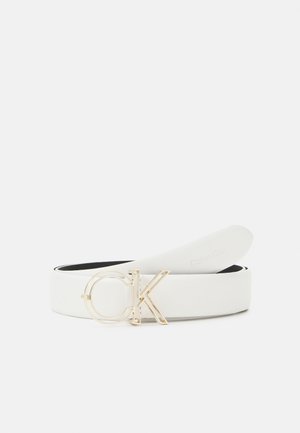 Bílý kožený pásek se zlatým přezkou "CK", částečně stočený na bílém pozadí.