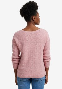 Rosa Strickpullover mit einem gewellten Texturmuster, weitem U-Boot-Ausschnitt und langen Ärmeln. Getragen mit blauen Jeans, von hinten betrachtet.