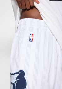 Shorts de baschet albe cu dungi verticale, un logo de urs în nuanță de navy și un insignă NBA. Talie elastică pentru confort și ajustare.