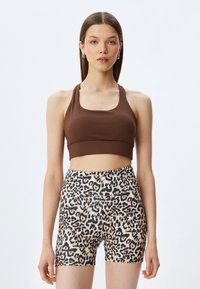 Brun crop top parret med leopardmønstret shorts med høj talje. Toppen har en rund halsudskæring, og shortsene har en glat og strækbar tekstur.