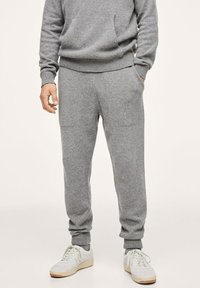 Grijze gebreide sweatshirt met bijpassende broek, voorzien van geribbelde boorden, een relaxte pasvorm en zijzakken. Afgemaakt met witte sport schoenen.